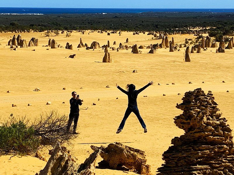 Two walkers dwarfed by the pillars on the Pinnacles Desert sand